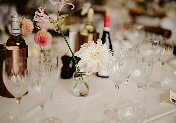 The wedding table set with numerous wine glasses, wine bottles, and flower decorations in small vases was a picturesque scene that any wedding photographer would love to capture.