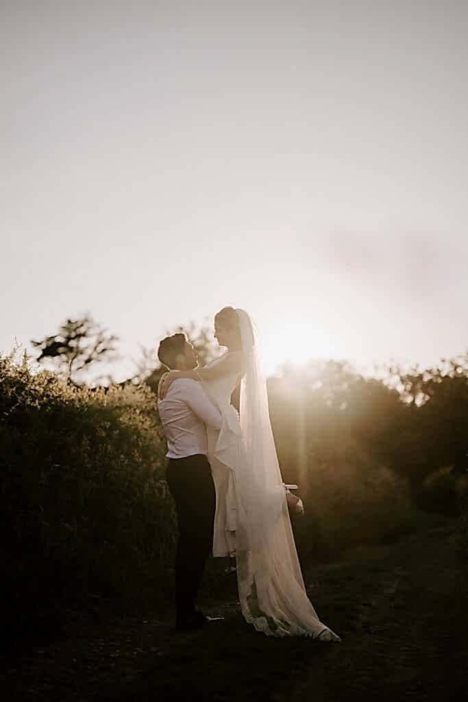 Couple embracing at sunset, wedding dress glowing.